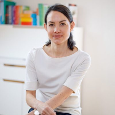 Mercedes Mende vor Bücherregal Mercedes Mende sitzt vor einem Bücherregal